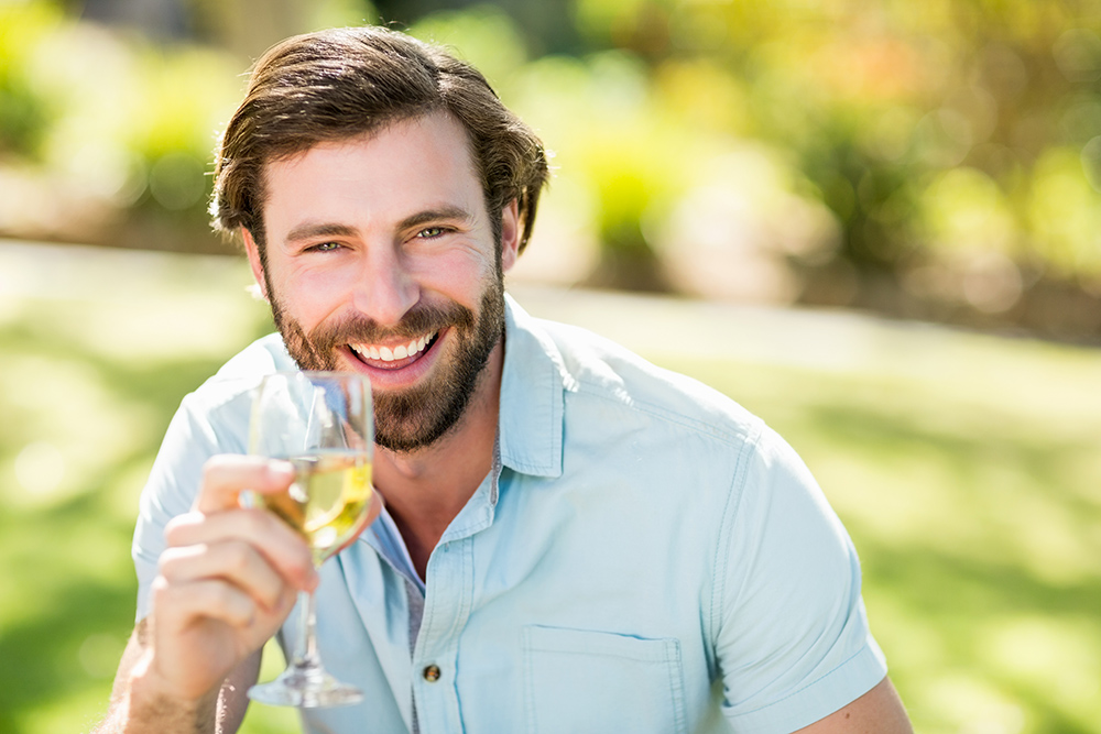 Portrait of man holding wine glass and smiling in park